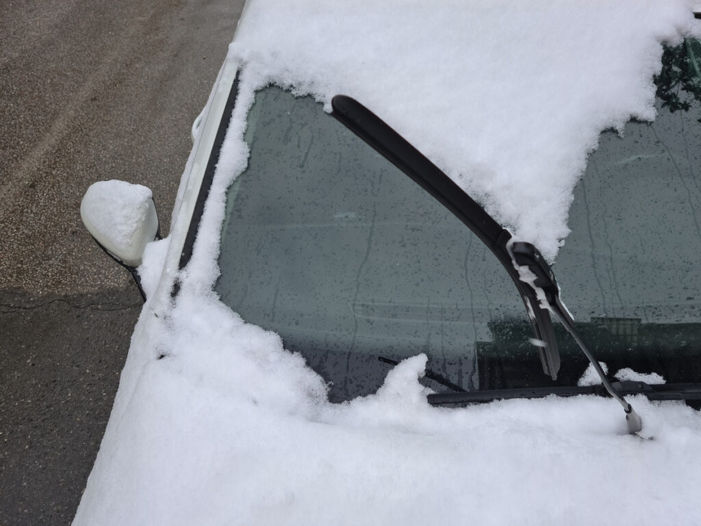 A photo of a car windshield, with snow being moved by a windshield wiper.